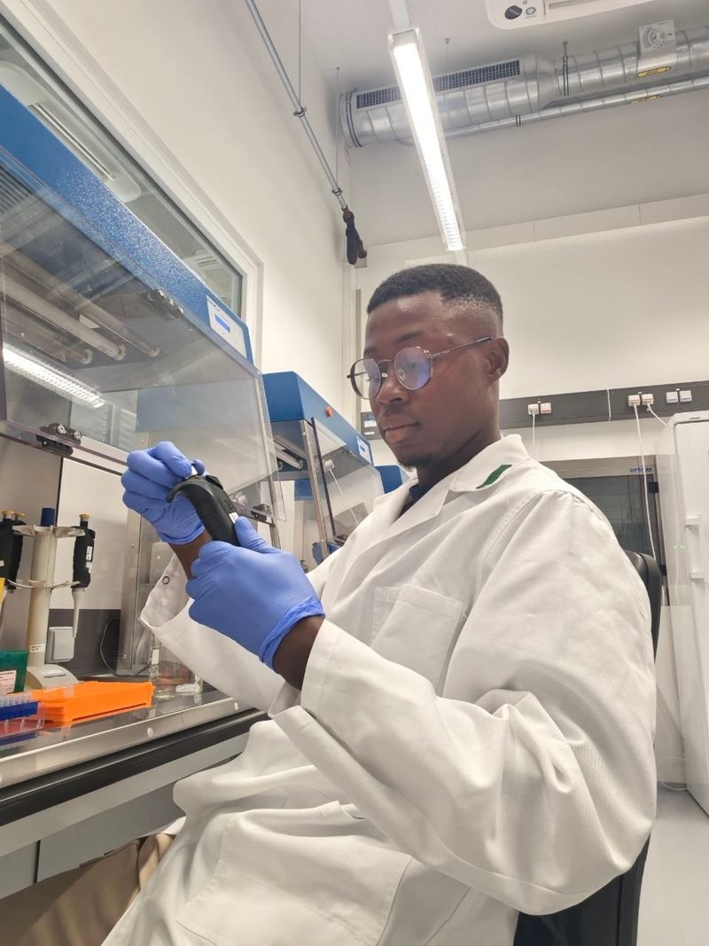 Freddy Konan en blouse blanche et gants, une pipette à la main, au laboratoire